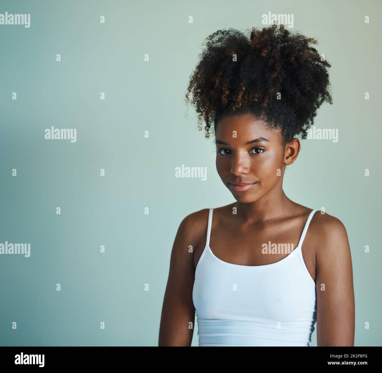 Ihr natürliches Haar bringt ihr schönes Gesicht hervor. Studioaufnahme einer schönen, frisch gesichtigen jungen Frau, die vor grünem Hintergrund posiert. Stockfoto