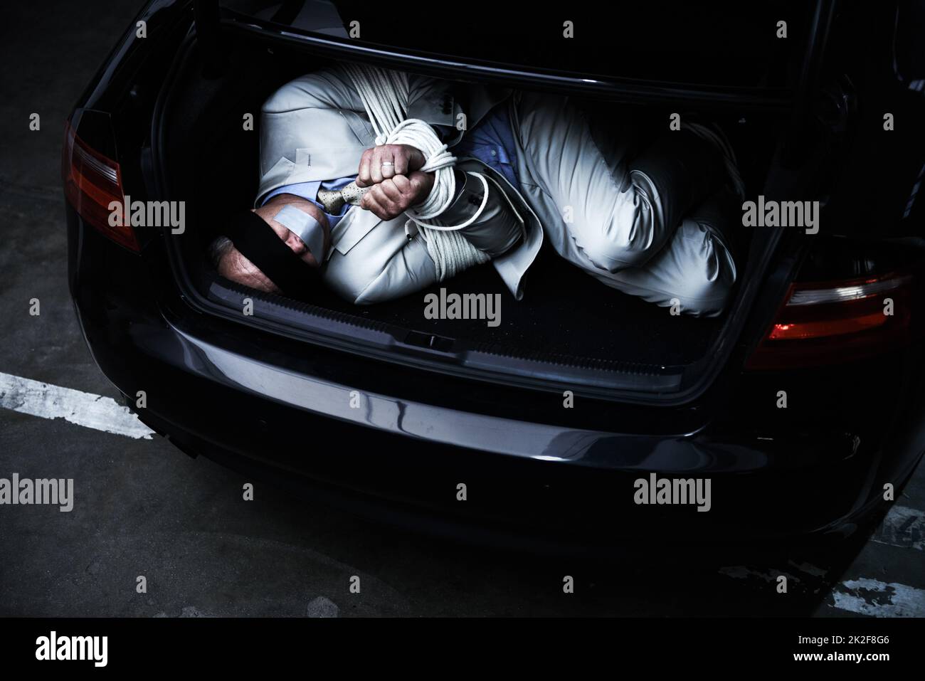 Hoffnung auf ein Wunder. Ein gebundener und mit verbundenen Augen im Kofferraum eines Autos liegender Geschäftsmann. Stockfoto