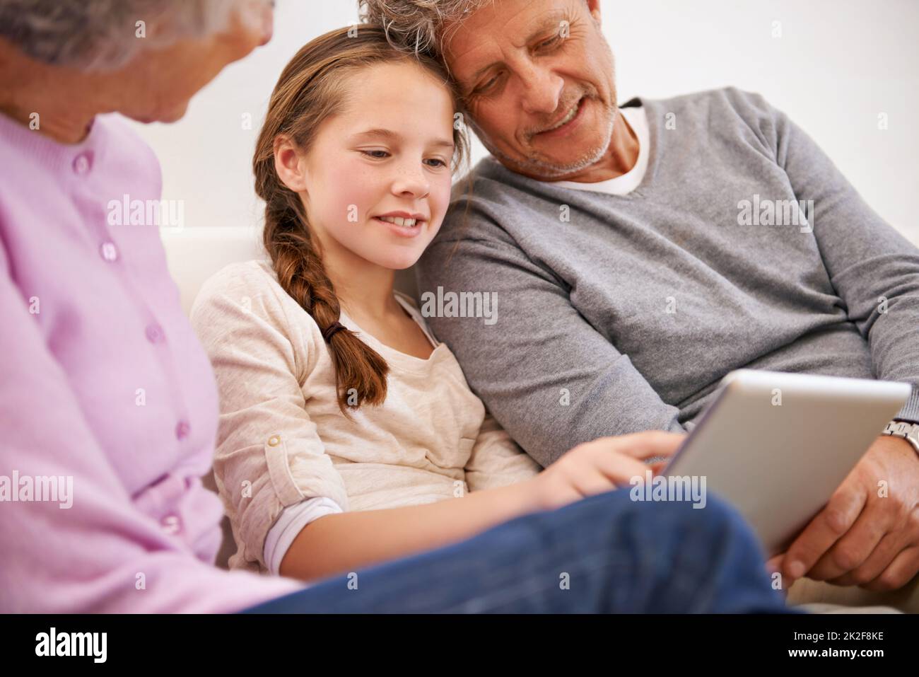 Und das ist die Welt der sozialen Medien. Aufnahme von Großeltern, die ihre Enkelin mit einem digitalen Tablet beobachten. Stockfoto