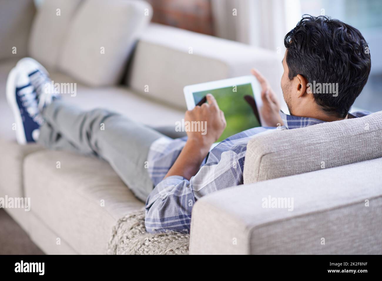 Zum Springen antippen. Eine kurze Aufnahme eines jungen Mannes, der sein Tablet benutzt, während er sich zu Hause entspannt. Stockfoto