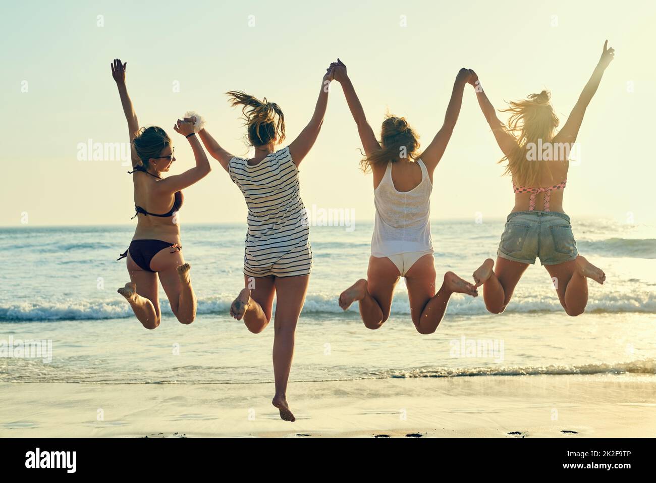 Strandtage sind die besten Tage. Rückansicht der besten Freundinnen, die am Strand in der Luft springen. Stockfoto