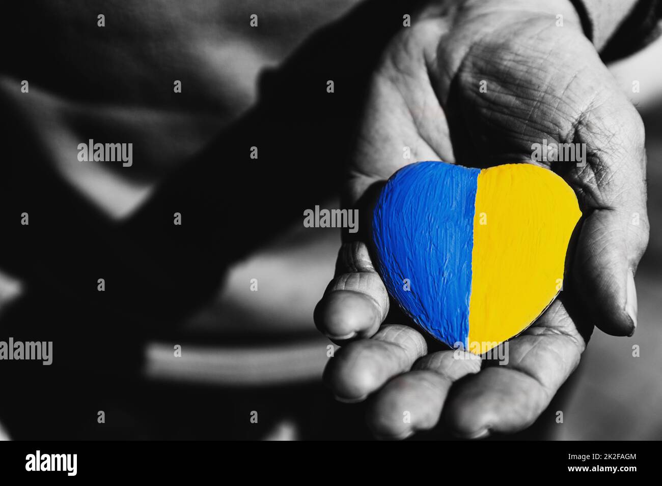 Seniorenhände oder Soldatenhände mit herzförmigem Stein bemalt mit ukrainischer Flagge Stockfoto