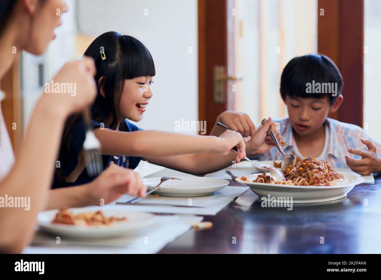 Ich bin Sekunden lang da. Aufnahme von zwei kleinen Kindern, die mit ihrer Mutter zu Hause essen. Stockfoto