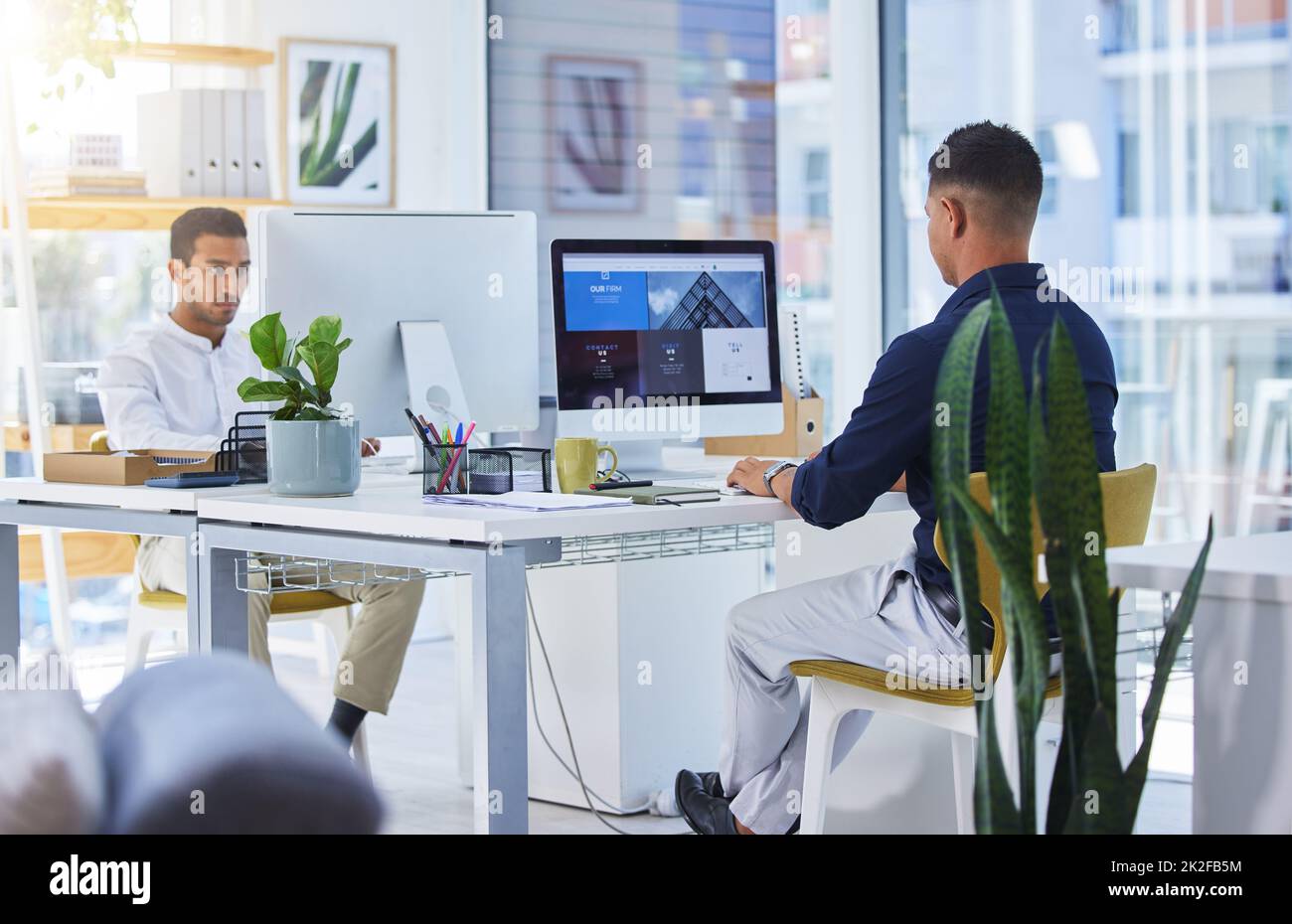 Sie wissen, wie Sie uns erreichen können. Aufnahme von zwei Männern, die in einem modernen Büro an ihren Computern arbeiten. Stockfoto