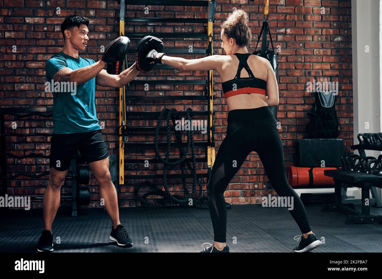 Ihre Stanztechnik ist erstaunlich. Eine kurze Aufnahme einer attraktiven jungen Boxerin, die mit ihrem Personal Trainer in einem Fitnessstudio trainiert. Stockfoto