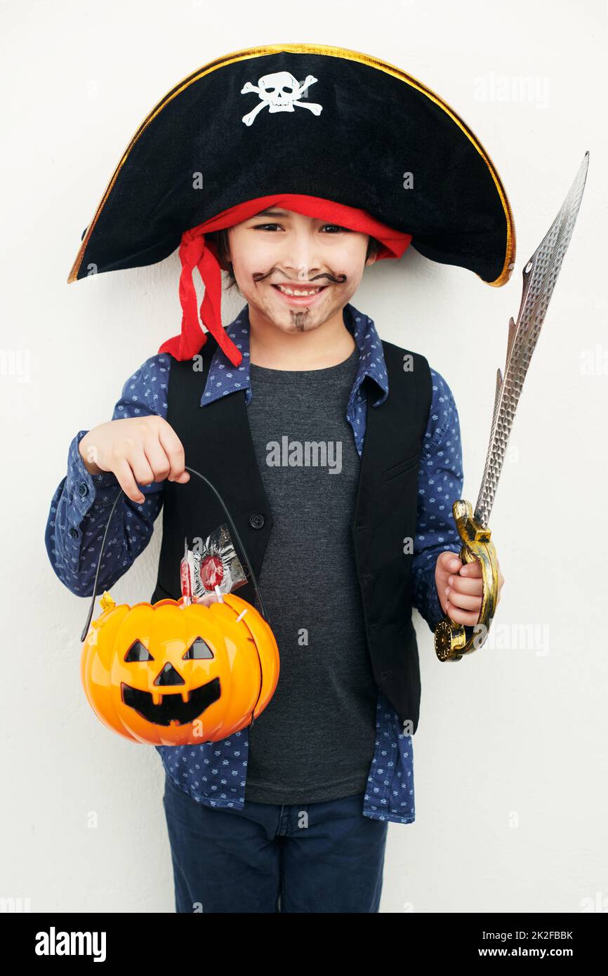 Verspielter Pirat. Aufnahme eines kleinen Jungen, der in einem Piratenkostüm gekleidet ist, während er einen Buben oder eine Laterne vor einem weißen Hintergrund hält. Stockfoto