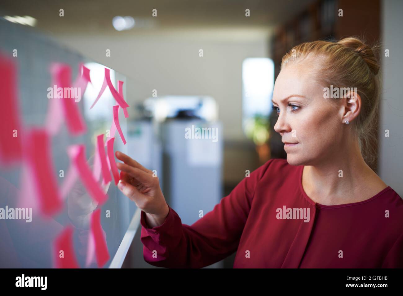 Überprüfung der Aufgaben für den Tag. Eine kurze Aufnahme einer attraktiven Geschäftsfrau, die die Aufgaben auf der Haftnotiztafel überprüft. Stockfoto