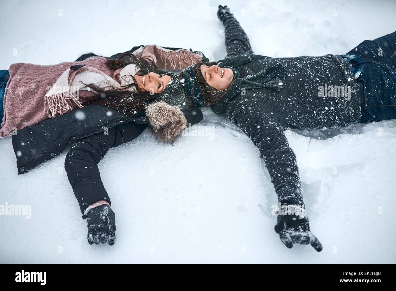 Der Schnee lässt uns wieder wie Kinder fühlen. High-Angle-Aufnahme eines Paares, das im Schnee liegt und Schneeengel macht. Stockfoto