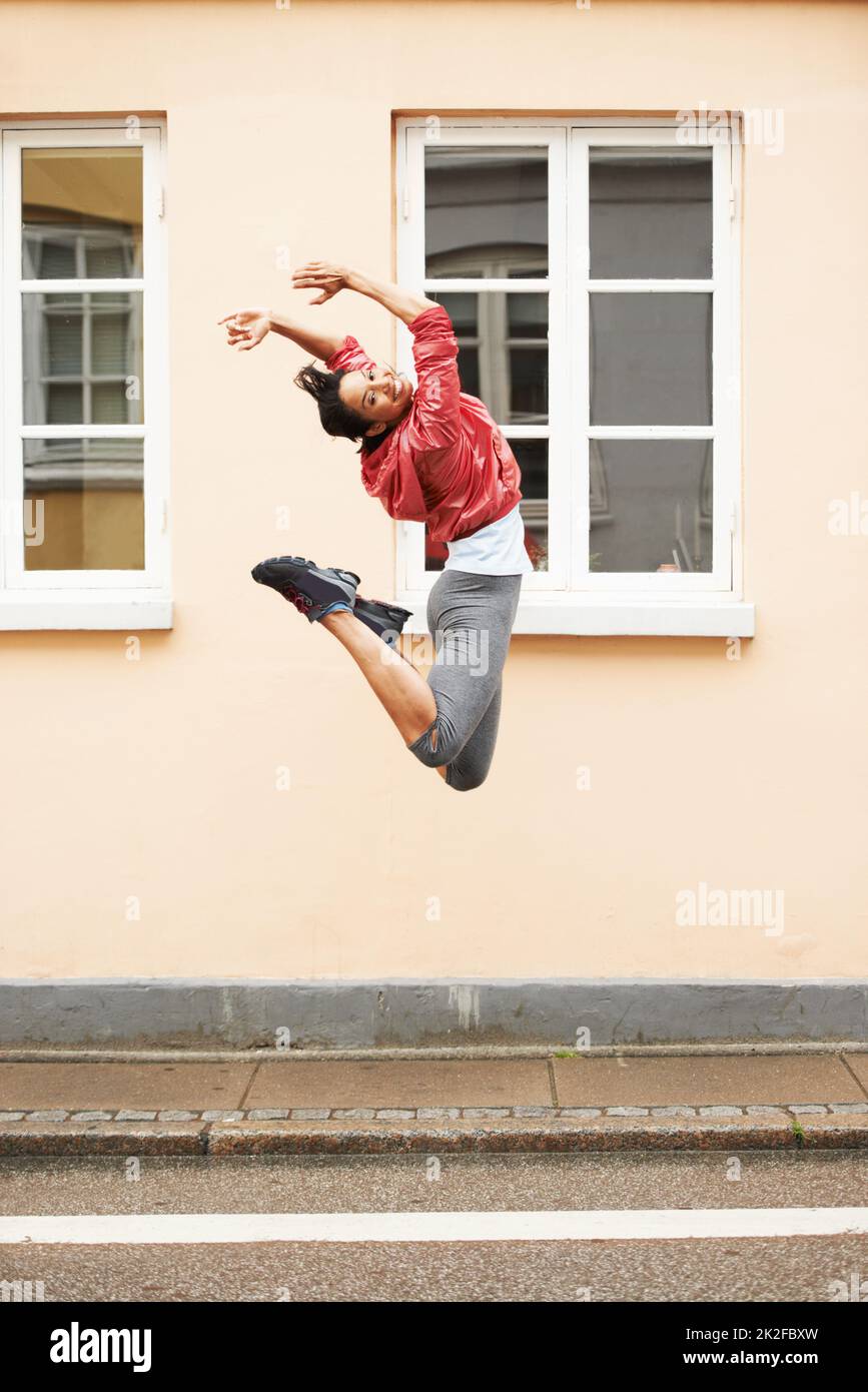 Voller Energie. Eine energische junge Frau in urbaner Sportkleidung, die auf der Straße springt. Stockfoto