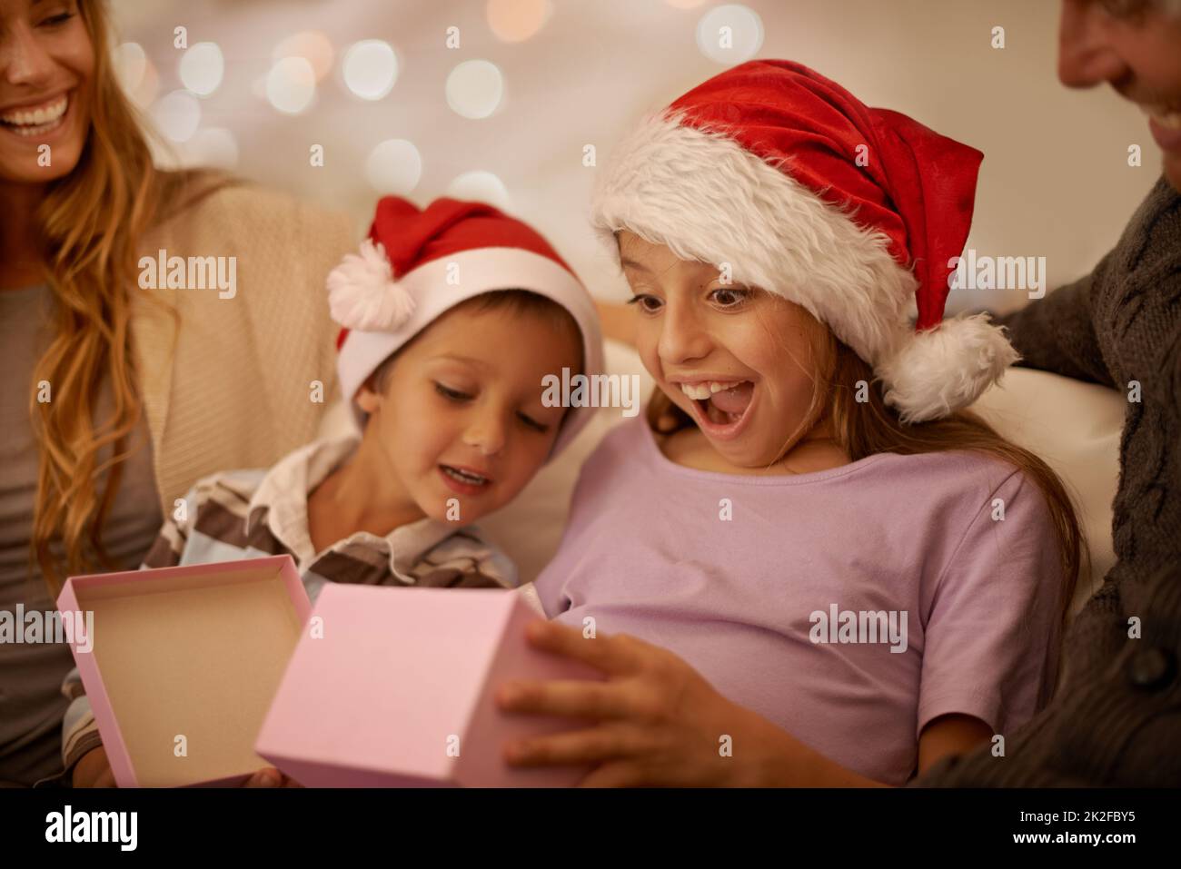 Genau das, was ich wollte. Ein kleines Mädchen wickelte ein Weihnachtsgeschenk aus, während es von ihrer Familie umgeben war. Stockfoto