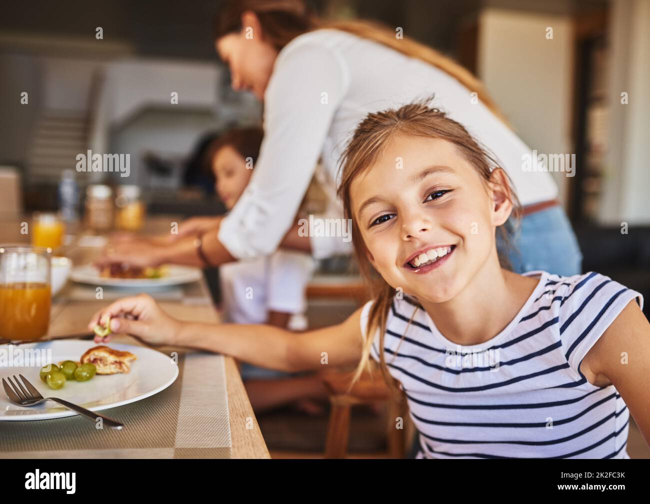 Genießen Sie ein köstliches Frühstück mit ihren Lieblingsmenschen. Portrait eines kleinen Mädchens, das im Hintergrund mit ihrer Familie frühstückt. Stockfoto