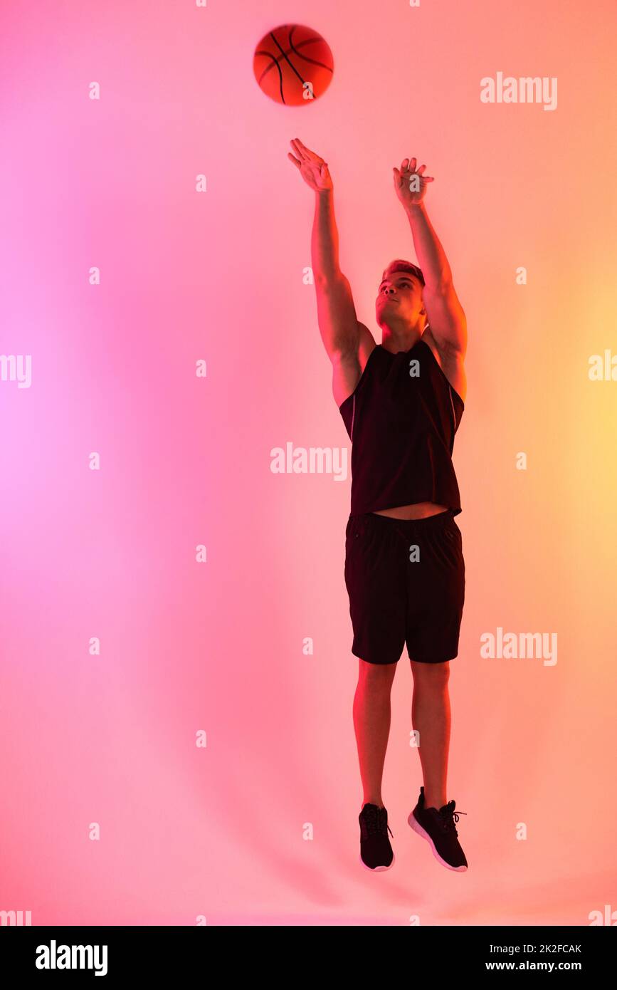 Schießen Sie Ihre Aufnahme. Studio-Aufnahme eines hübschen jungen Basketballspielers, der einen Sprung gegen einen mehrfarbigen Hintergrund schiebt. Stockfoto
