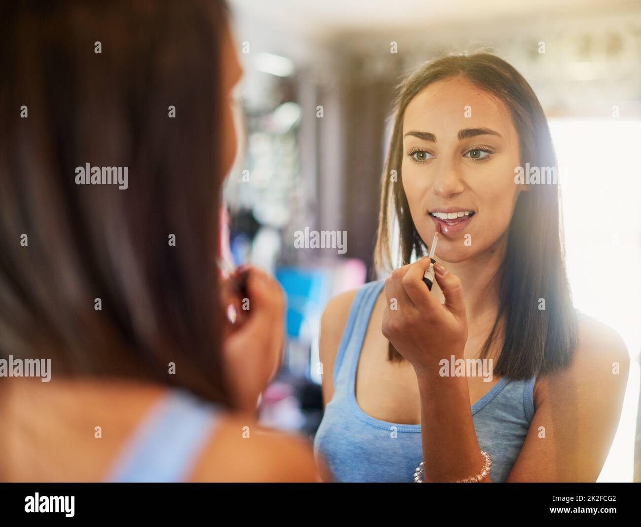 Akzentuiert ihre bereits perfekten Lippen. Aufnahme einer attraktiven jungen Frau, die zu Hause Lipgloss in einen Spiegel applite. Stockfoto