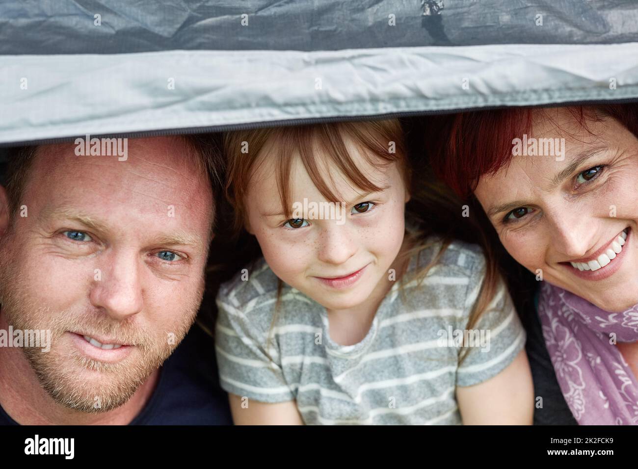 Flucht in die freie Natur als Familie. Porträt eines niedlichen kleinen Mädchens und ihrer Eltern, die zusammen in einem Zelt sitzen. Stockfoto