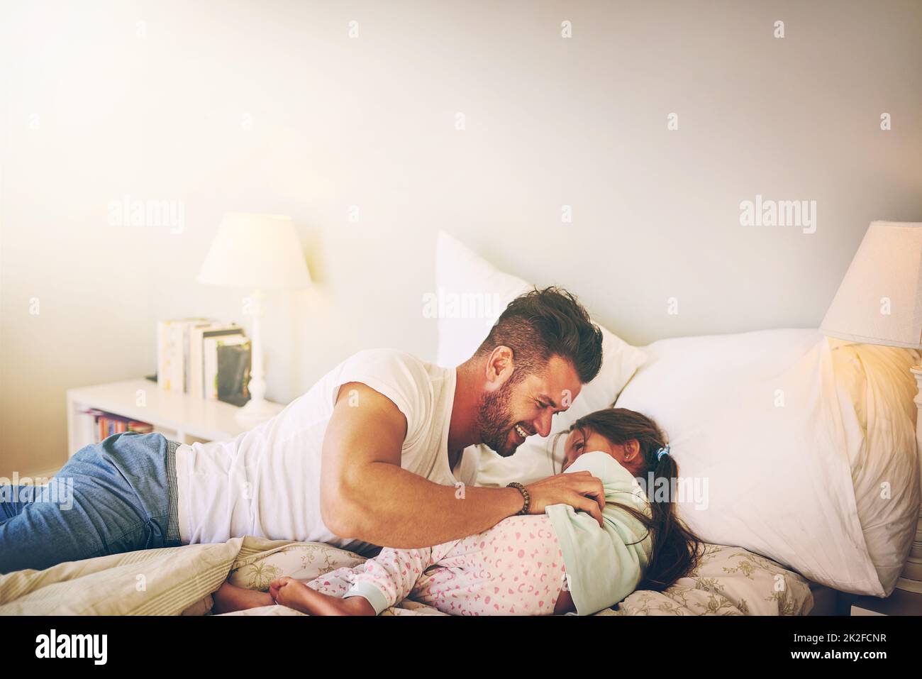 Zu Hause mit Papa. Aufnahme eines fröhlichen Vaters und einer Tochter, die zu Hause einen Kitzelkampf auf dem Bett führen. Stockfoto