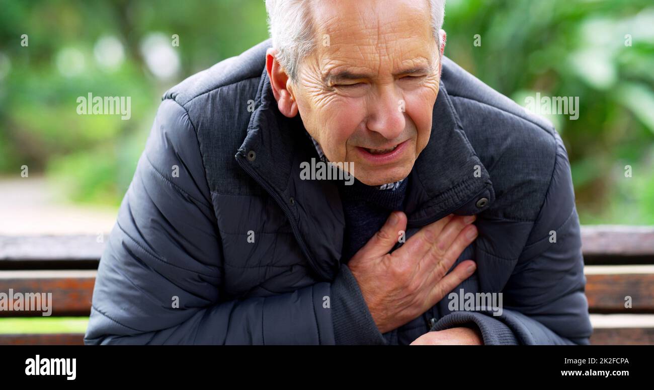 Was ist los? Ausgeschnittene Aufnahme eines gestressten älteren Mannes, der auf einer Bank saß und seine Brust in einem Park unter Unwohlsein hielt. Stockfoto