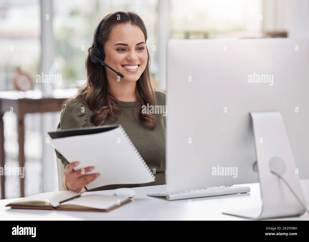 Eingabe neuer Informationen in das System. Aufnahme eines jungen Callcenter-Agenten, der während der Arbeit an einem Computer in einem Büro Papierkram durchläuft. Stockfoto
