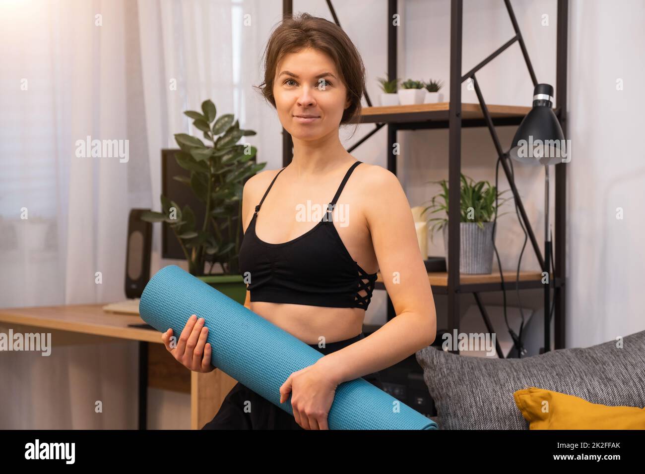 Das Porträt einer athletischen jungen Frau mit einer Sportmatte in den Händen ist bereit zum Training. Stockfoto