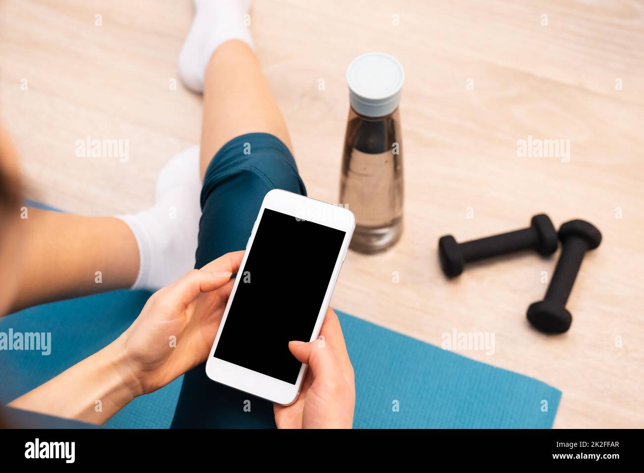 Rückansicht einer sportlichen Frau, die auf dem Boden ruht, mit einem modernen Smartphone. Modell Stockfoto