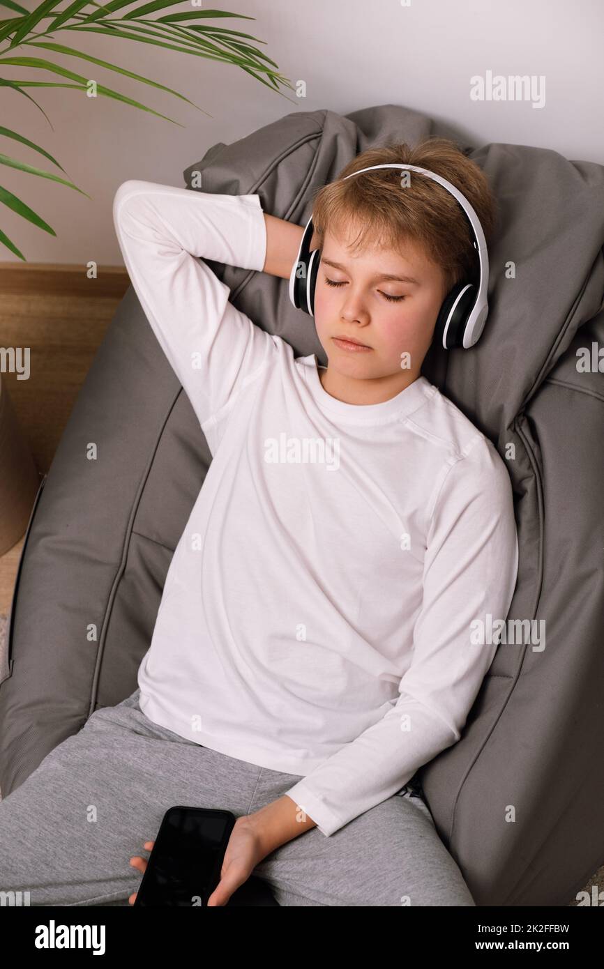 Entspannter Teenager, der auf einem rahmenlosen Sitzsack mit Kopfhörern sitzt. Weißes T-Shirt-Modell Stockfoto