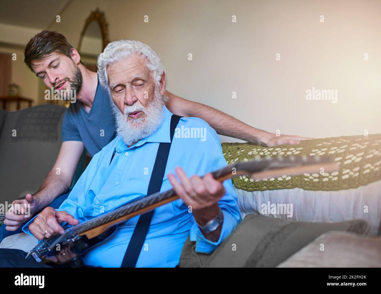 Du bist nie zu alt, um ein Rockstar zu werden. Aufnahme eines glücklichen jungen Mannes, der seinem älteren Großvater beibringt, zu Hause auf der Couch E-Gitarre zu spielen. Stockfoto