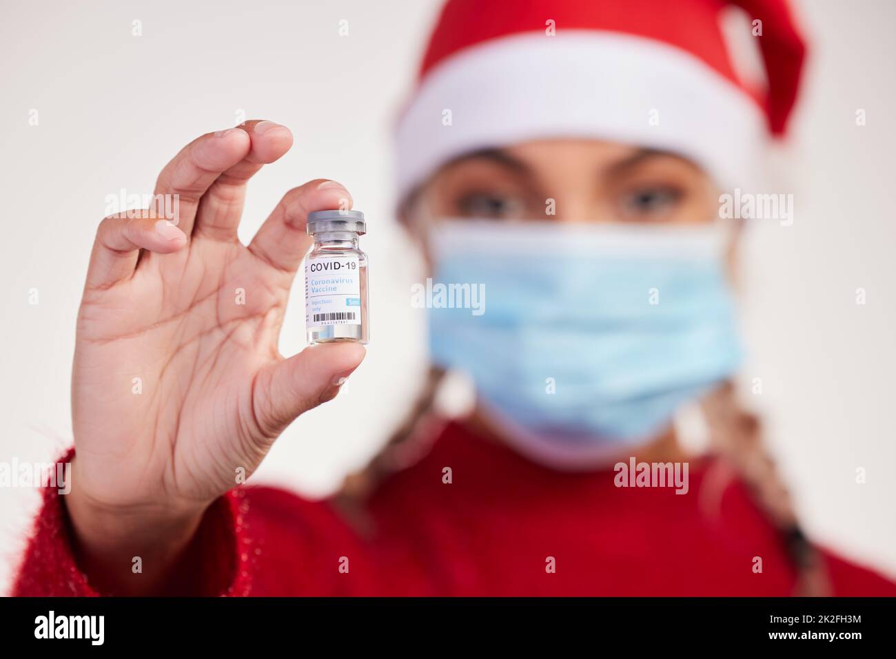 Alles, was ich zu Weihnachten will, ist ein Impfstoff. Studioaufnahme einer jungen Frau, die einen Impfstoff hält und eine Maske vor grauem Hintergrund trägt. Stockfoto