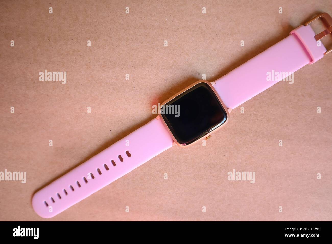 Kabellose Smartwatch mit pinkfarbenem Band isoliert auf braunem Hintergrund aus Kraftpapier Stockfoto