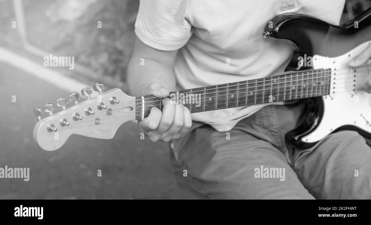 Schwarzweißfoto eines jungen Mannes, der Gitarre spielt, Nahaufnahme, Konzentration auf die Finger Stockfoto