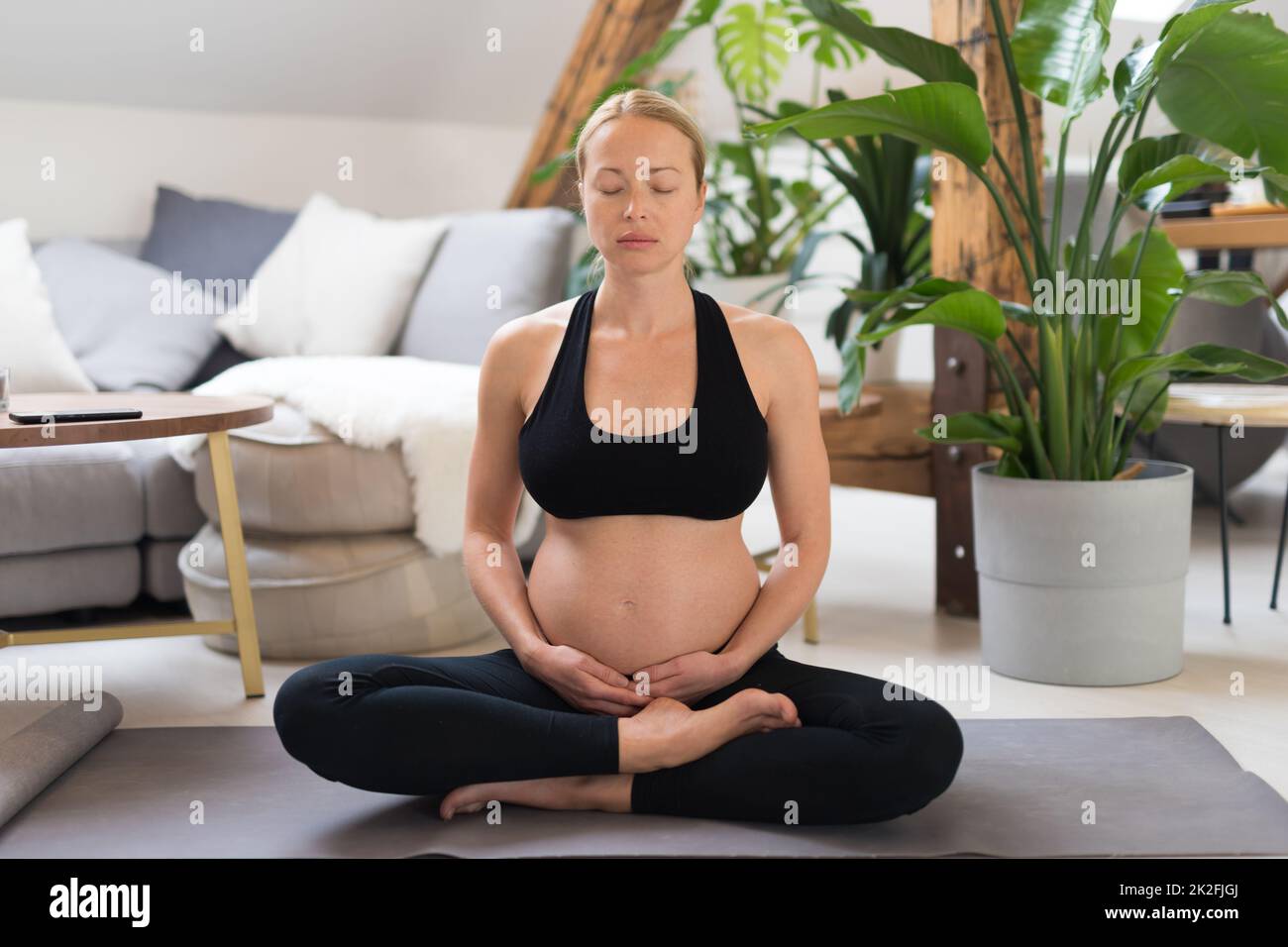 Junge, schöne, schwangere Frau, die Yoga trainiert, ihren Bauch streichelt. Junge, fröhlich, erwartungsvoll, entspannt, denkt an ihr Baby und genießt ihr zukünftiges Leben. Mutterschaft, Schwangerschaft, Yoga-Konzept. Stockfoto