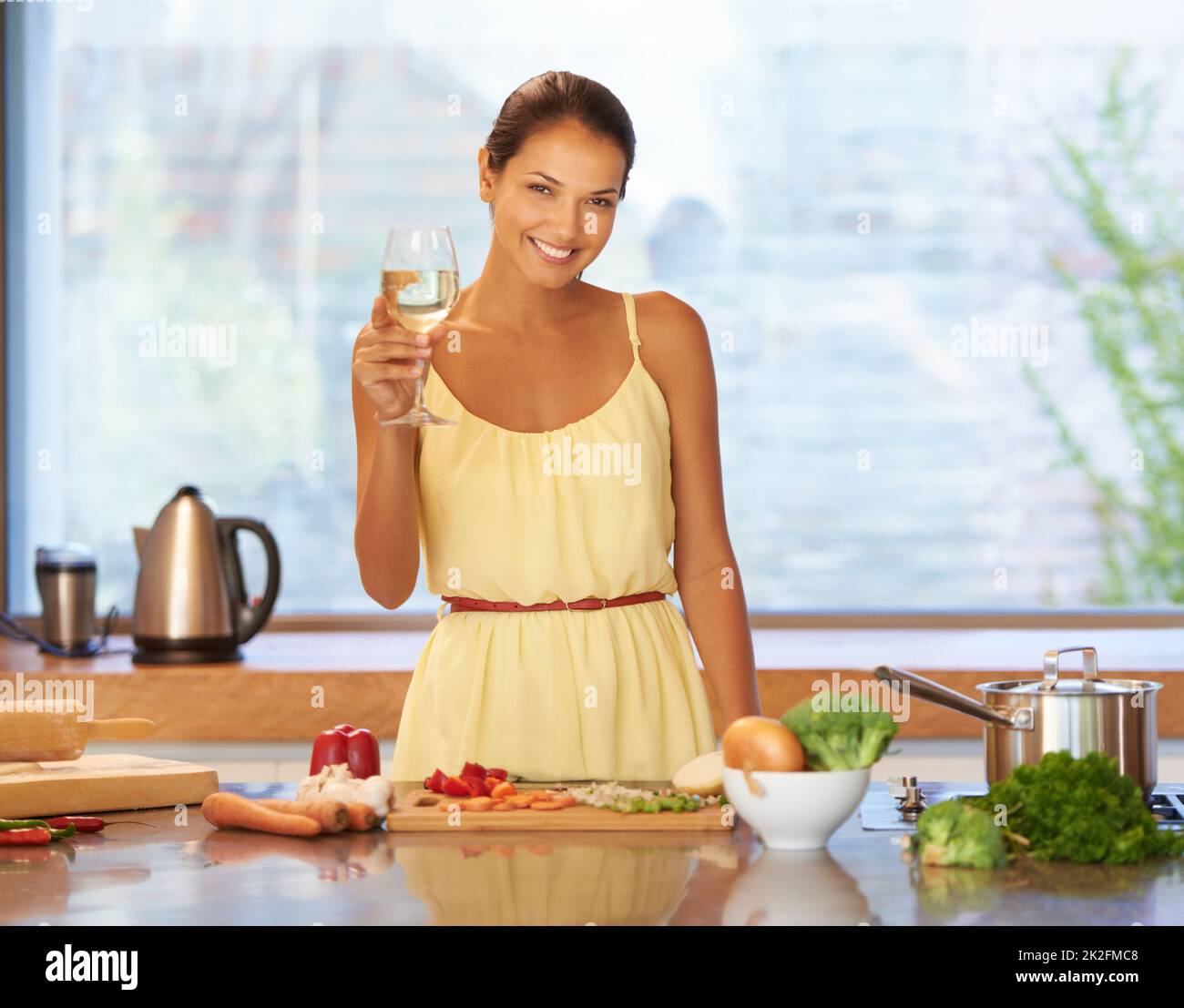 Prost zu gutem Essen. Eine junge Frau, die beim Kochen ein Glas Wein in der Hand hält. Stockfoto
