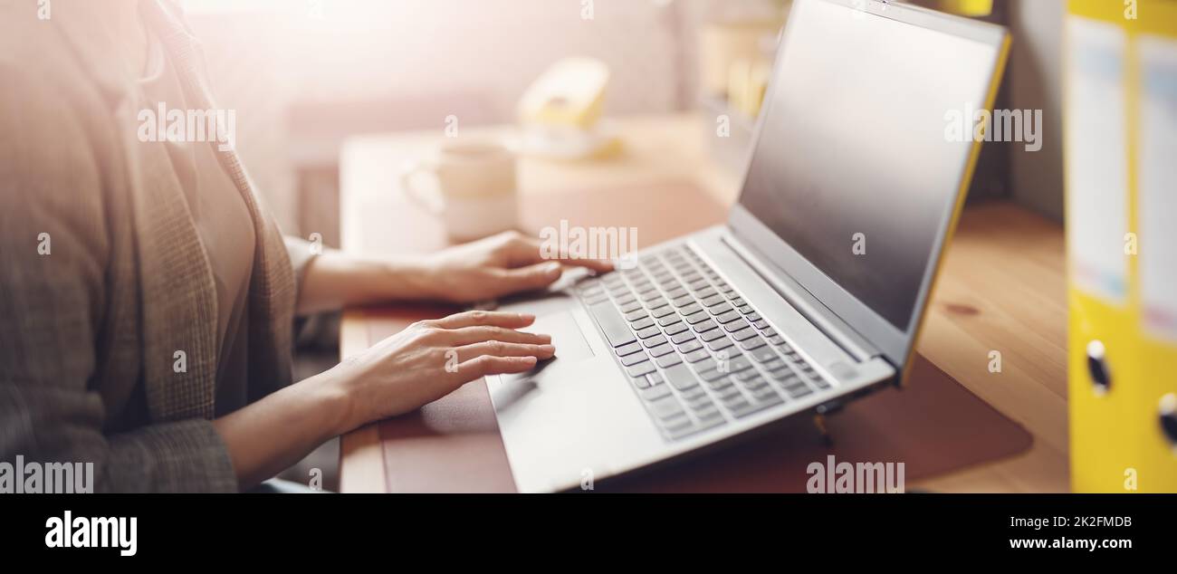 Frau mit Smartphone in der Hand, die im Büro am Laptop arbeitet Stockfoto
