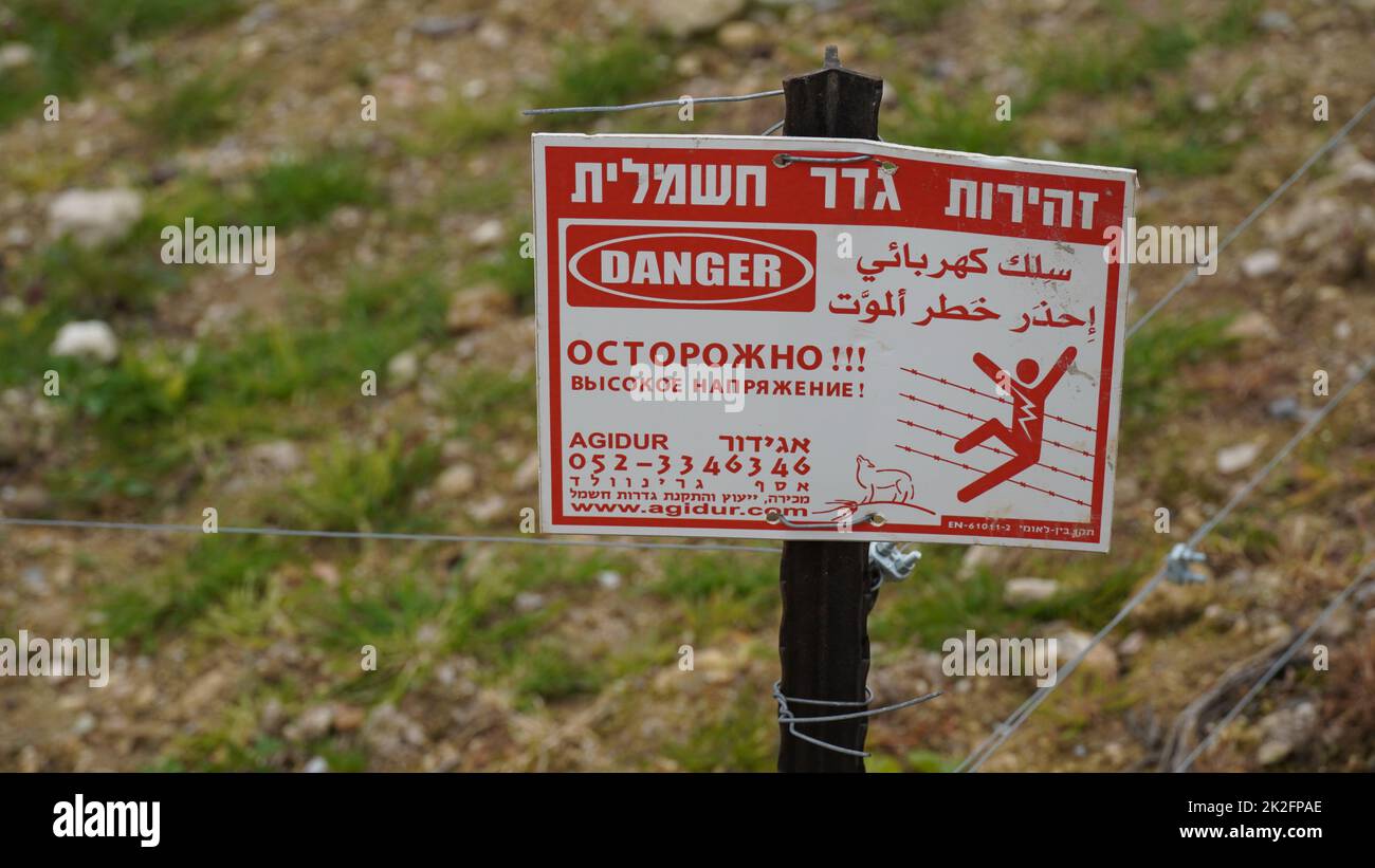 Warnschild Elektrozaun. Geschrieben in drei Sprachen - Hebräisch, Russisch, Englisch. Todeswarnung Stockfoto