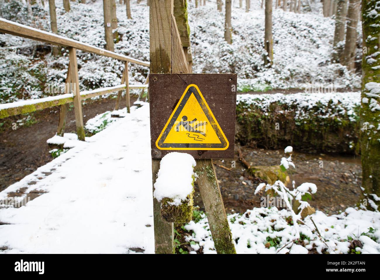 Rutschiges Warnschild im Wald, Holzbrücke mit Schnee bedeckt, Wintersaison, Vorsicht vor Gefahr, im Freien Stockfoto