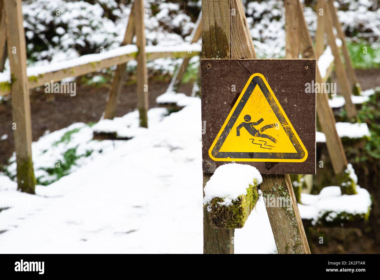 Rutschiges Warnschild im Wald, Holzbrücke mit Schnee bedeckt, Wintersaison, Vorsicht vor Gefahr, im Freien Stockfoto
