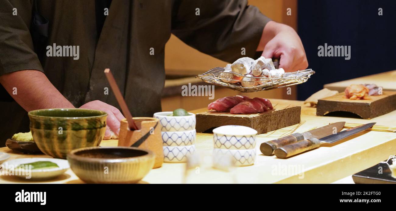 Koch brennt Thunfisch mit heißer Holzkohle. Genießen Sie das Omakase-Erlebnis im japanischen Sushi-Restaurant. Stockfoto