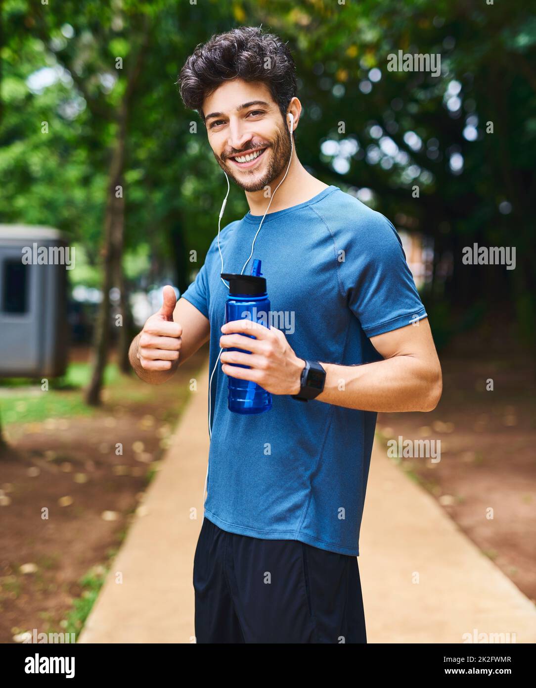 Du bist gut auf dem Weg zu einem besseren Lebensstil. Porträt eines sportlichen jungen Mannes, der eine Wasserflasche hält und beim Training im Freien Daumen nach oben zeigt. Stockfoto