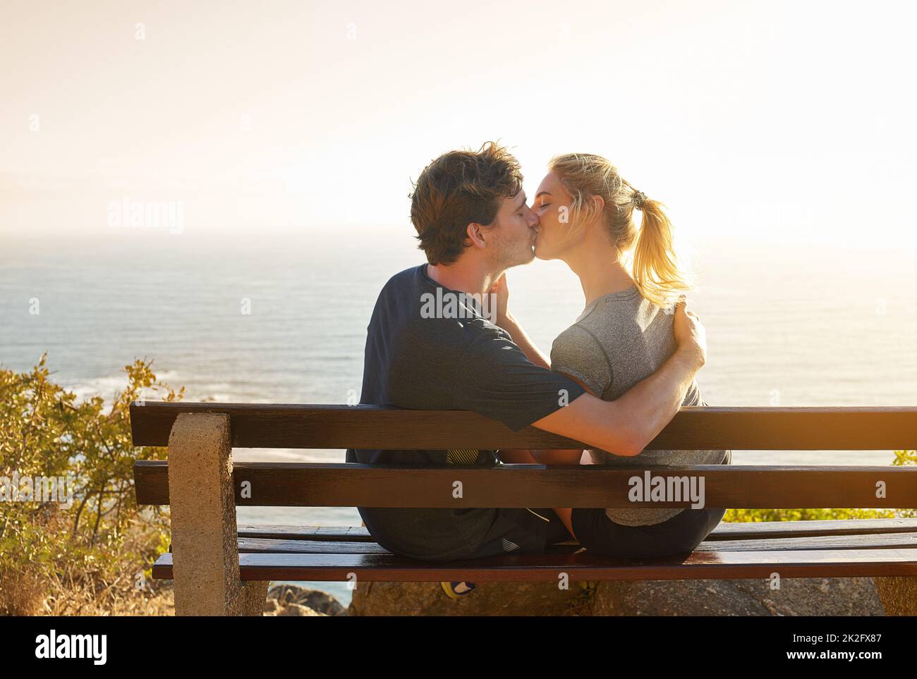 Dieser Kuss ist immer schöner als die Aussicht. Aufnahme eines liebevollen Paares, das auf einer Bank mit Blick auf das Meer sitzt. Stockfoto