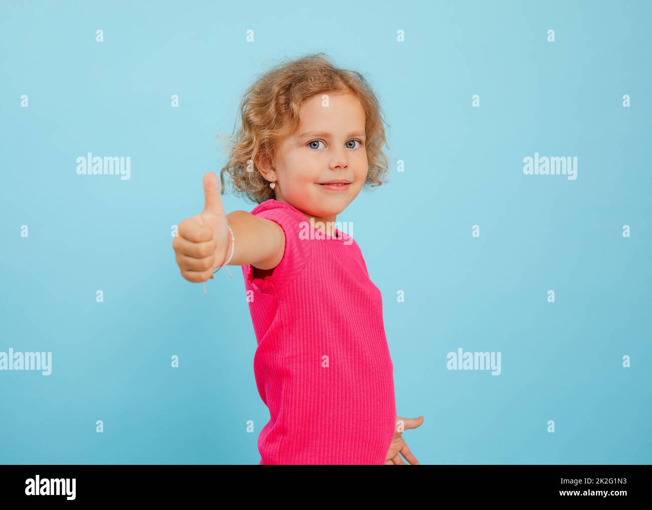 Charmantes kleines Mädchen stehen mit Finger nach oben auf ausgestrecktem Arm auf leerem blauen Hintergrund, kopieren Raum. Foto von glücklichen Kind im Kindergartenalter mit Stockfoto