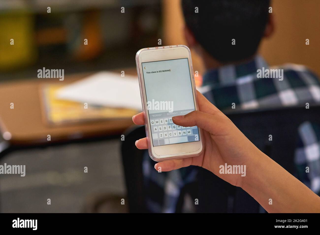 Nicht gerade von dem Unterrichts-Plan fasziniert. Aufnahme einer unidentifizierbaren Schülerin, die ihr Smartphone in der Klasse benutzt. Stockfoto