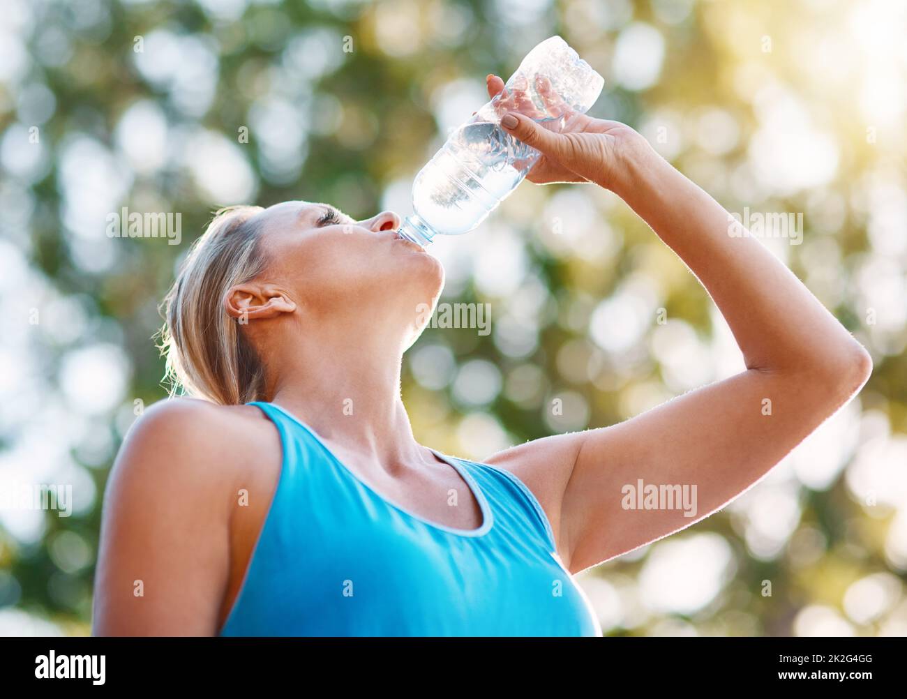 Bleib während deines Workouts immer hydratisiert. Low-Angle-Aufnahme einer reifen Frau, die im Freien Wasser aus einer Flasche trinkt. Stockfoto