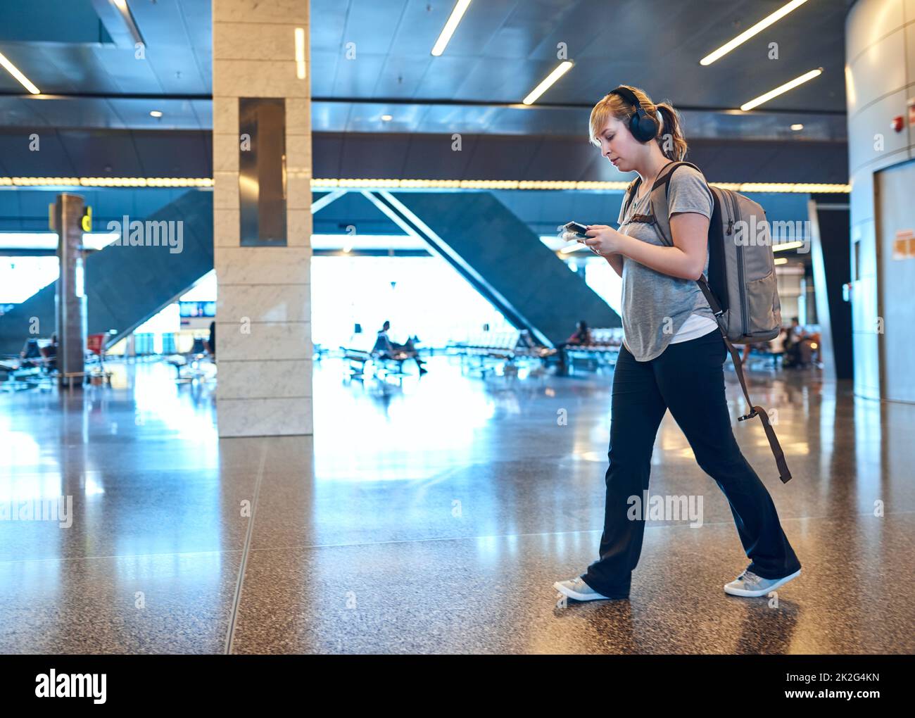 Wir gingen zur Abflughalle. In voller Länge eine attraktive junge Frau, die einen Text sendet, während sie durch einen Flughafen läuft. Stockfoto