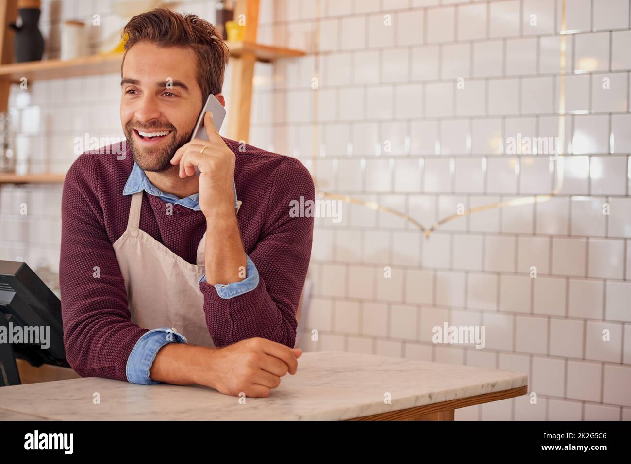 Bei seinen Lieferanten einchecken. Aufnahme eines glücklichen Geschäftsinhabers, der sein Smartphone benutzte, während er sich an die Theke in seinem Café lehnte. Stockfoto