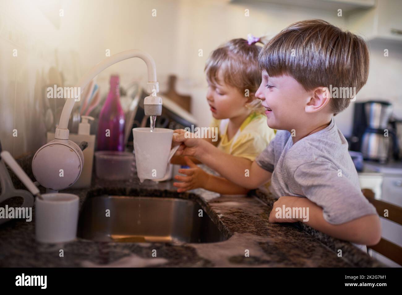 Sie werden super sauber sein, wenn sie fertig sind. Aufnahme von zwei liebenswerten kleinen Geschwistern, die in der Küche zu Hause gemeinsam Geschirr waschen. Stockfoto