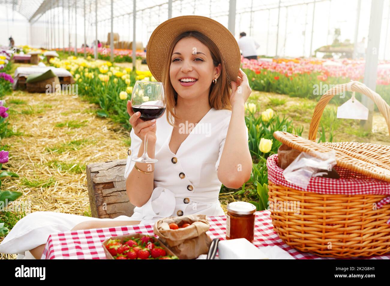Attraktive junge Frau mit Vorspeise unter Tulpenblüten. Frische Ernte mit Picknick und Rotwein im Frühjahr am Land. Stockfoto