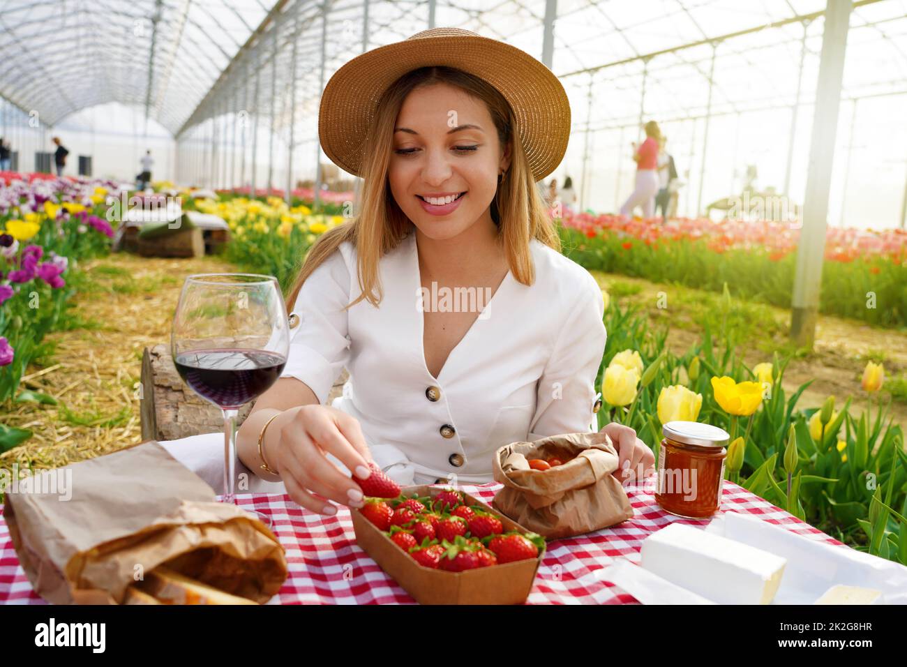 Schöne junge Frau mit Picknick. Mädchen nimmt eine Erdbeere. Frische Ernte auf dem Land im Frühling. Stockfoto