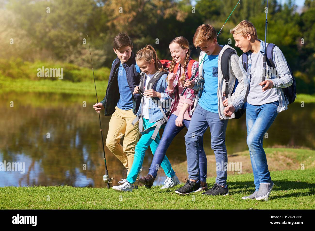 Outdoor-Abenteuer mit Freunden. Eine Gruppe junger Freunde, die Rucksäcke tragen, läuft zusammen an einem See entlang. Stockfoto