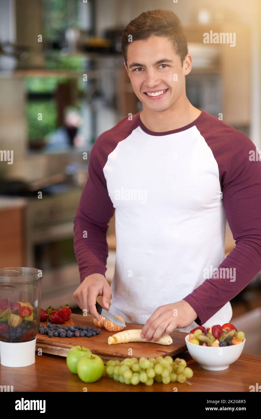 Es ist schmackhaft und nahrhaft. Porträt eines glücklichen jungen Mannes, der in seiner Küche zu Hause ein gesundes Früchtefrühstück zubereitet. Stockfoto