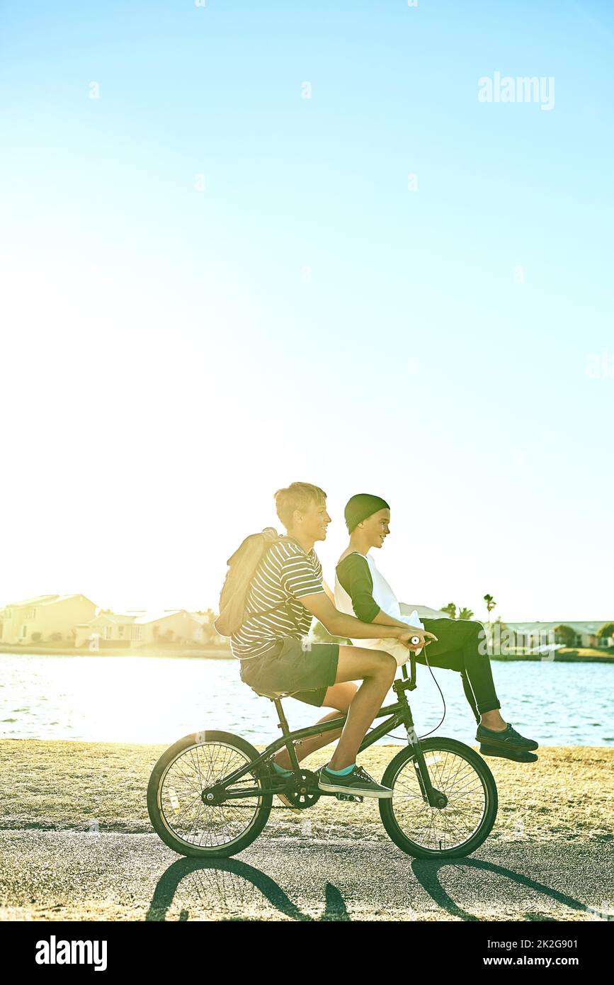 Er brauchte einen Aufzug. In voller Länge ein kleiner Junge, der seinem jüngeren Bruder einen Aufzug auf einem Fahrrad draußen gab. Stockfoto