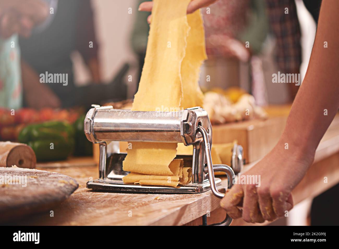 Das Nudelgericht ins Rollen bringen. Ein kurzer Schuss einer Person, die frisch gebackenen Teig durch eine Nudelmaschine rollt. Stockfoto