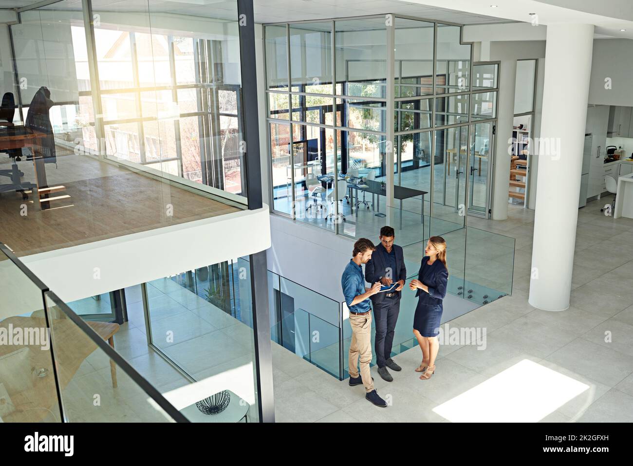 Moderne Unternehmen brauchen moderne Denker. Aufnahme von drei Kollegen, die sich über ein digitales Tablet unterhalten, während sie in einem modernen Büro stehen. Stockfoto